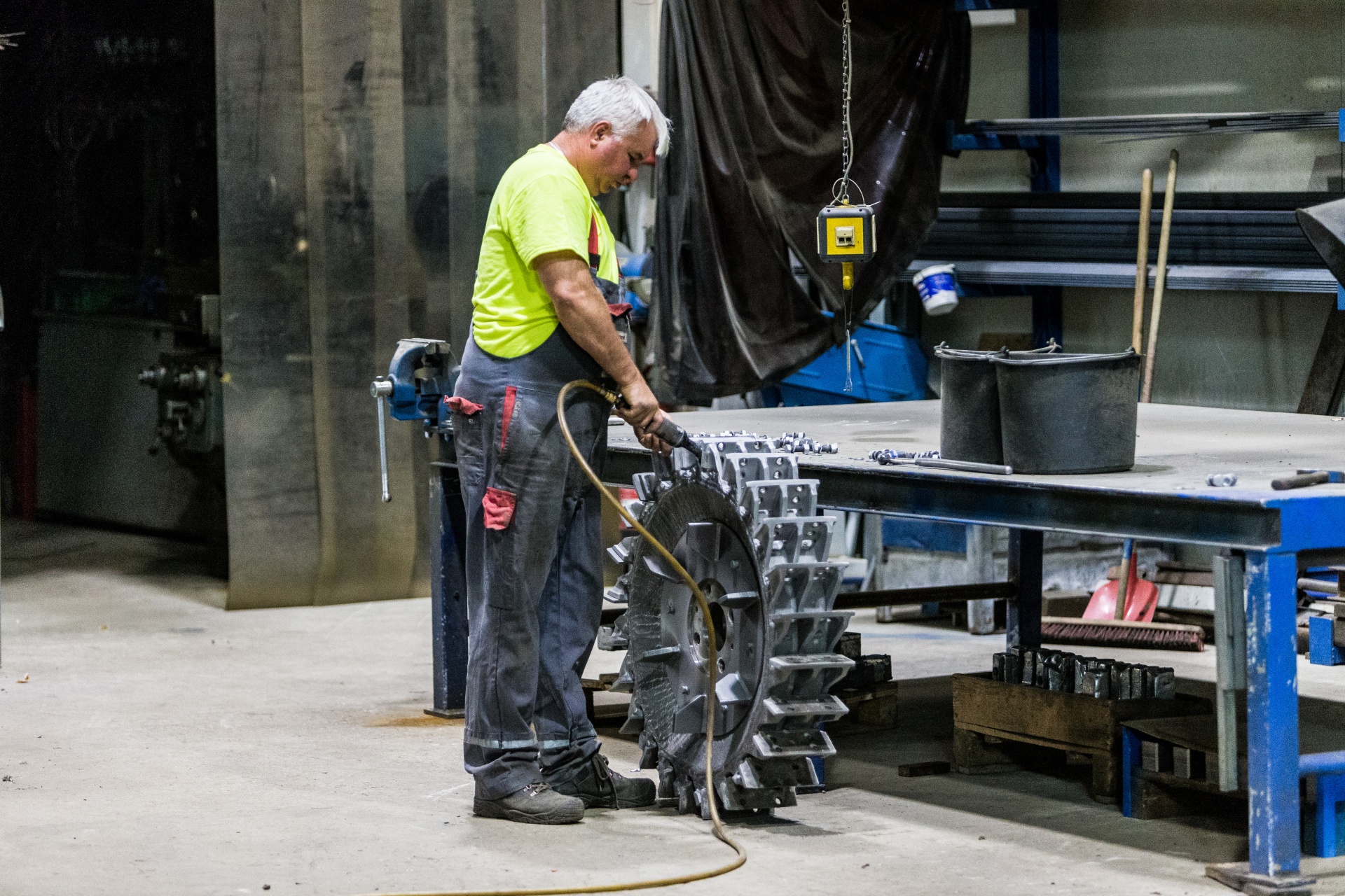 Ein Arbeiter in einer Produktionshalle in leuchtenden Klamotten, während er Ersatzteile für Recyclingmaschinen bearbeitet.