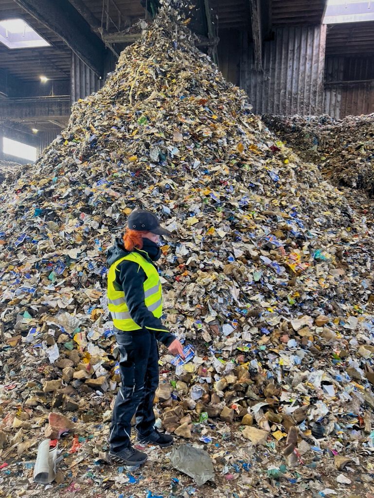 Mitarbeiterin begutachtet einen großen Haufen sortierter Kunststoffabfälle in einer Recyclinganlage – typisches Inputmaterial für Zerkleinerer und Sortiertechnik