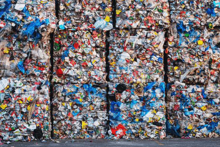 Gestapelte, gepresste Würfel aus recyceltem Plastik- und Metallmüll mit bunten Verpackungen, Plastikfolien und Dosen in einer Recyclinganlage.