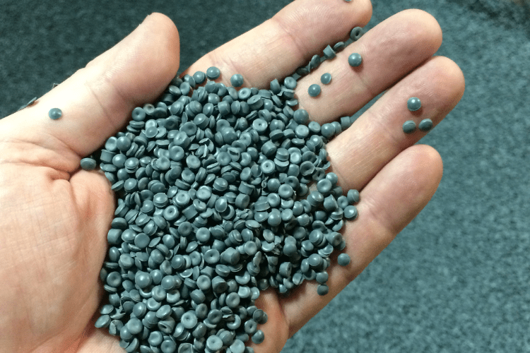 Dunkelgrünes Plastikgranulat wird in einer Hand gehalten. Im Hintergrund sieht man noch mehr von dem Granulat.