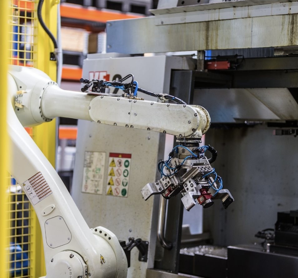 Weiße Maschine in unserer Produktionshalle. Im Hintergrund sieht man Regale, in denen optimierte Ersatzteile wie Gegenmesser, Siebe, Rotormesser, Statormesser, Schneidkronen etc. gelagert sind.
